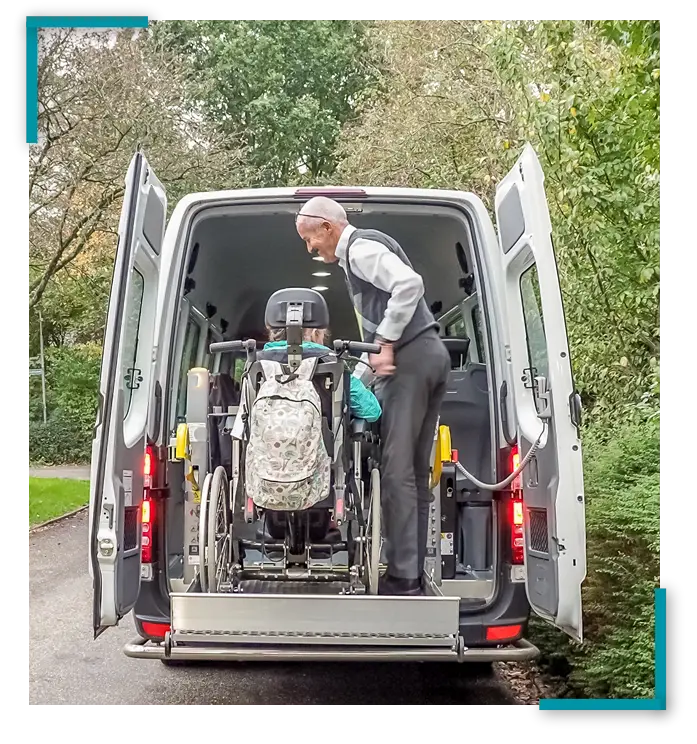 Oudere chauffeur assisteert dame in rolstoel met uitstappen aan de achterzijde van een aangepaste auto.